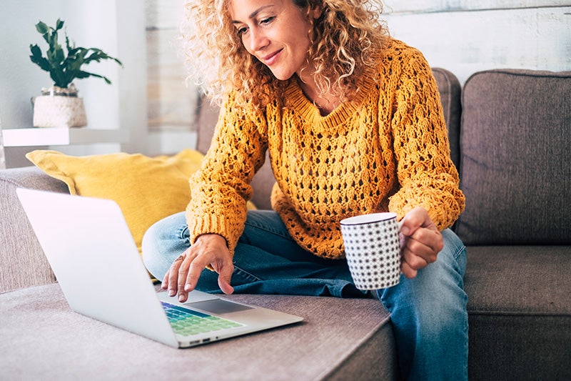 Woman on couch looking at her laptop screen while holding a mug